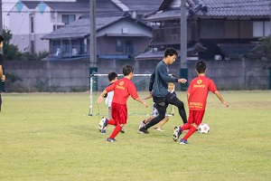 広大な芝生を走ってサッカーをする子どもたちと大学生の様子