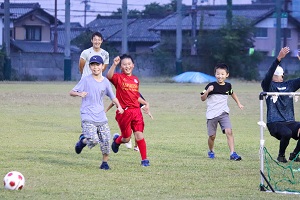 広大な芝生を走ってサッカーをする子どもたちと大学生の様子