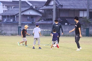 広大な芝生を走ってサッカーをする子どもたちと大学生の様子