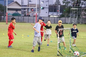 広大な芝生を走ってサッカーをする子どもたちと大学生の様子